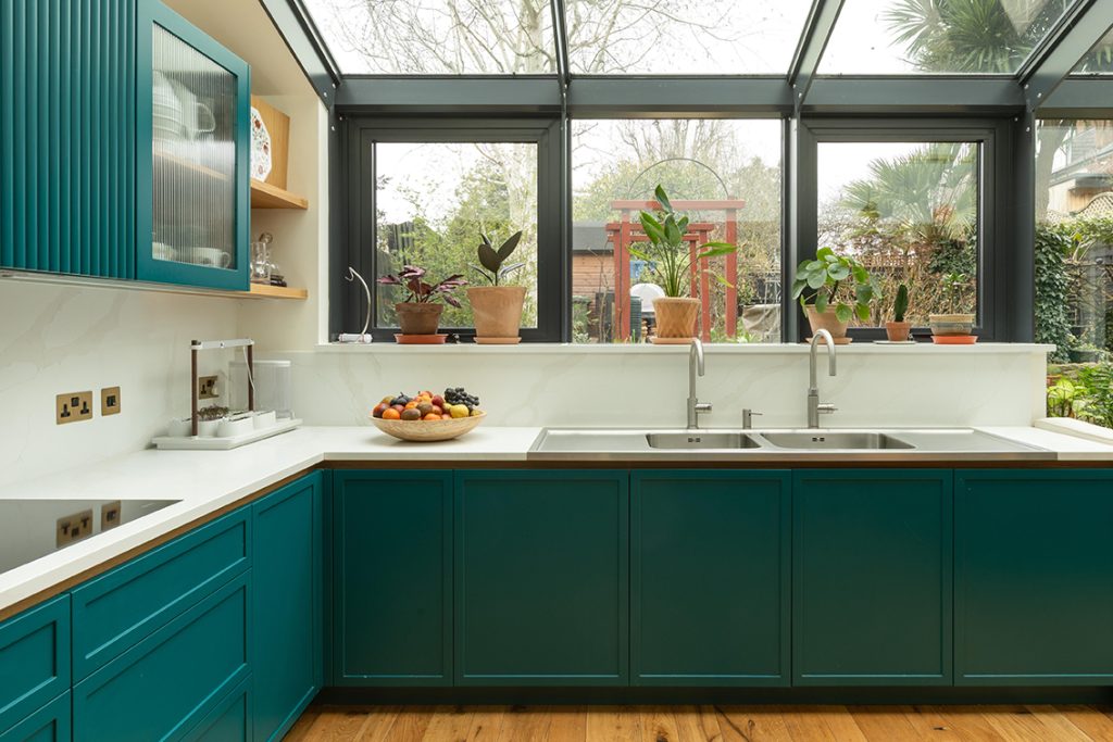 Custom-fabricated kitchen sink area with refined metal taps and a pale stone worktop in a bespoke Muswell Hill kitchen.