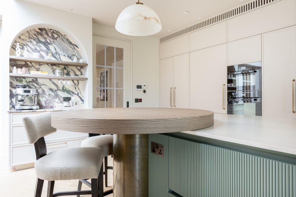 Elevated rounded breakfast table adjoining a curved kitchen island, creating informal family seating in Hampstead.