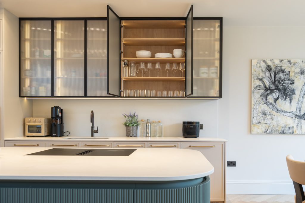 Elegant fluted glass wall cabinets with dark metal frames and integrated lighting above a pale kitchen worktop.