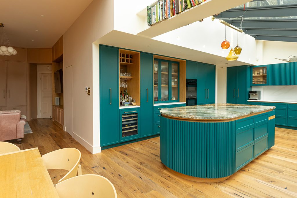 Sculptural teal kitchen island with curved fluted end panels and integrated lighting in a Muswell Hill family home.